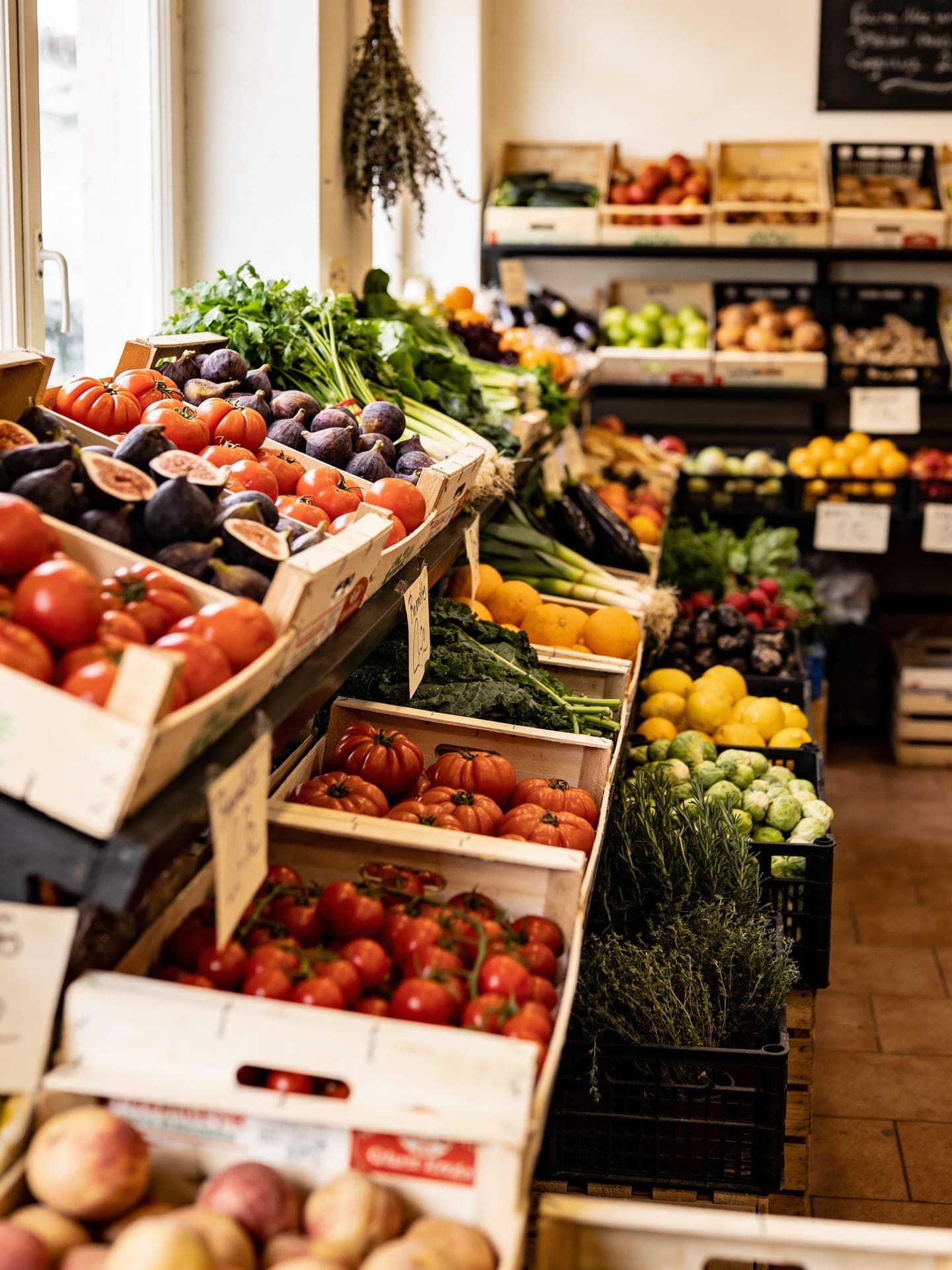 A produce market stall brimming with fresh seasonal vegetables, figs and herbs in warm daylight